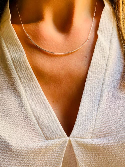 Vue de face gros plan tour de cou d'une femme avec le collier Emy composé d'une fine chaîne avec une barre courbée en argent