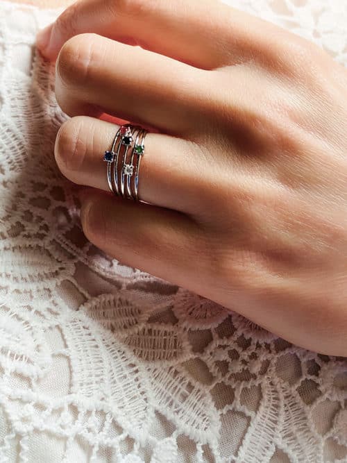 Gros plan main de femme avec la bague Nora en argent avec des pierres en zirconium de couleur.