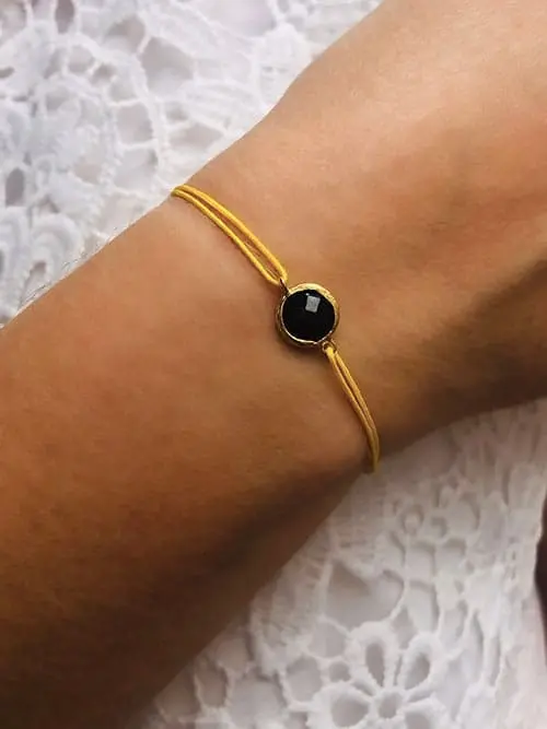 Gros plan poignet de femme avec un bracelet cordon avec une pierre semi précieuse d'onyx noir cerclée de plaqué or. Bijoux à personnaliser et fabriqués à la main