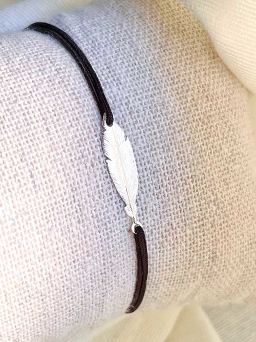 Gros plan sur un tissu blanc un bracelet cordon avec une plume ciselée en argent