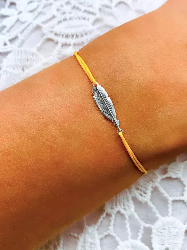 Gros plan poignet de femme avec un bracelet cordon avec une plume ciselée en argent. Bijoux à personnaliser et fabriqués à la main