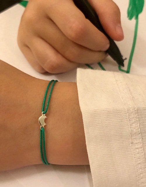 Gros plan mains d'enfant en train de dessiner avec au poignet le Bracelet cordon Petite Lune. Bijoux pour enfants en argent