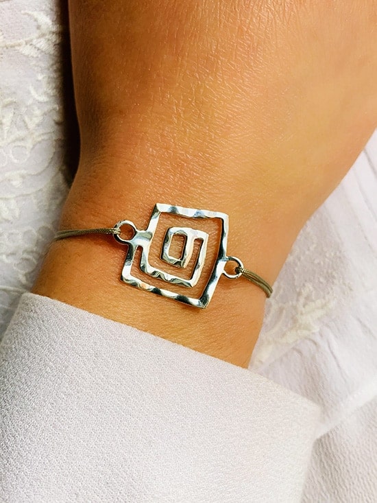 Gros plan poignet de femme avec le bracelet cordon Labyrinthe avec un cordon gris et une spirale de forme carrée en argent martelée