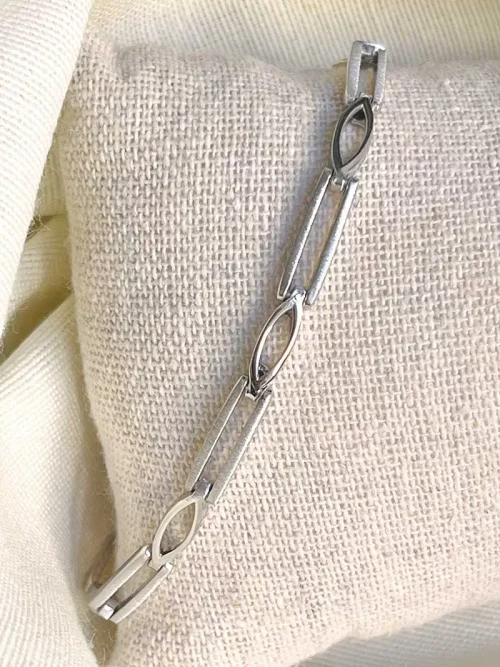Gros plan sur un tissu blanc le bracelet Albane avec des gros maillons rectangles et losanges en argent