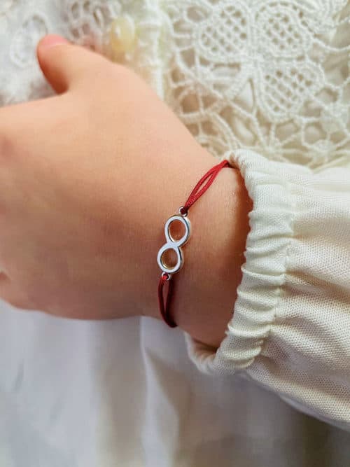 Vue 3/4 avant bracelet cordon rouge avec bijou en forme d'infini en argent porté sur poignet petite fille