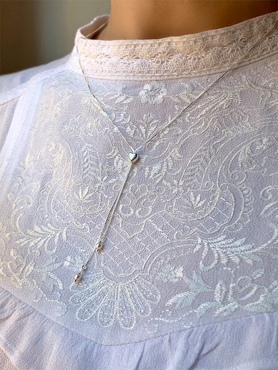 Gros plan cou de femme autour du cou le collier Louise en argent avec un pendentif long avec deux perles tenues par un coeur