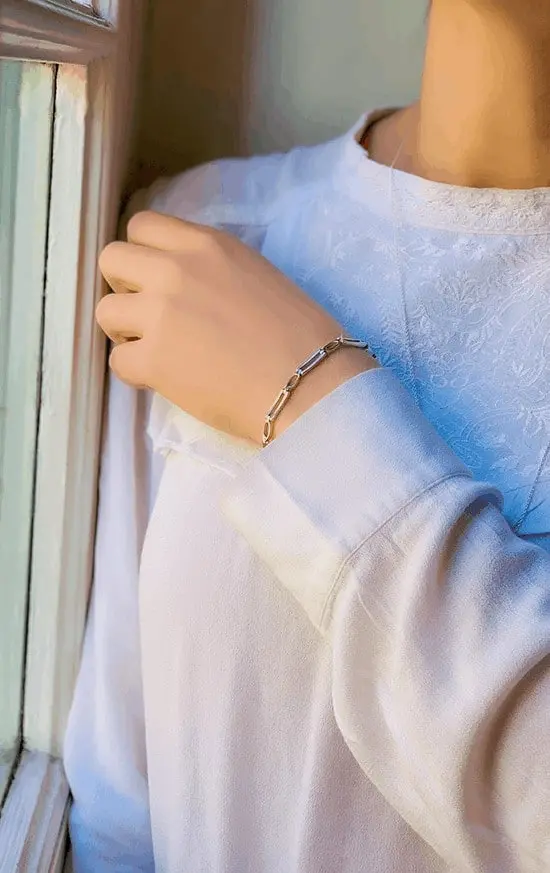 Vue de 3/4 d'une femme devant une fenêtre avec au poignet le bracelet Albane une chaîne avec de gros maillons rectangulaires et en losanges en argent et argent mat