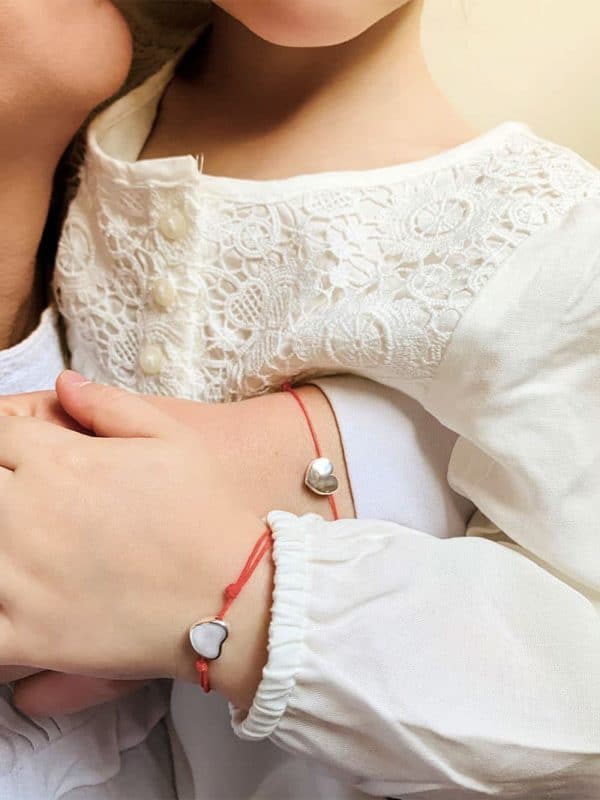 Vue de face une petite fille dans les bras de sa mère avec chacune au poignet le même bracelet. Elles portent un bracelet cordon avec un coeur coulissant en argent. Bracelet cordon Coeur et Bracelet cordon Petit Coeur
