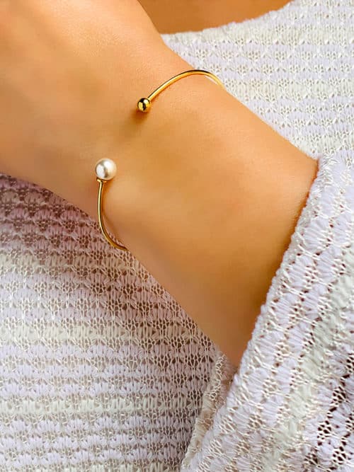 Vue de face poignet de femme avec le bracelet Olivia. Un jonc en plaqué or ouvert avec une perle et une perle en plaqué or