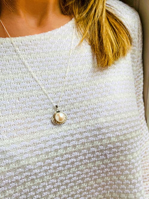 Gros plan buste de femme avec le collier Sofia à personnaliser selon la longueur de la chaîne, et son pendentif en forme de coquillage en argent avec une perle en son centre