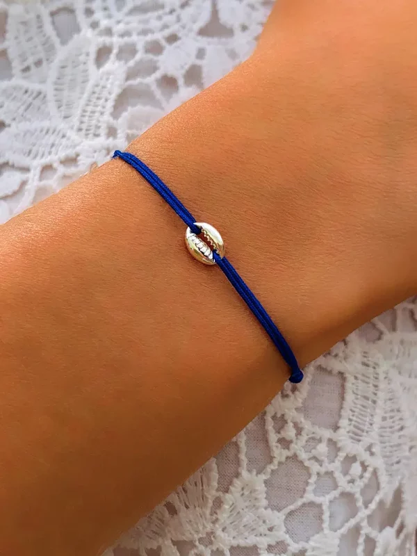 Gros plan poignet de femme avec un bracelet cordon avec un coquillage en argent. Bijoux à personnaliser et fabriqués à la main