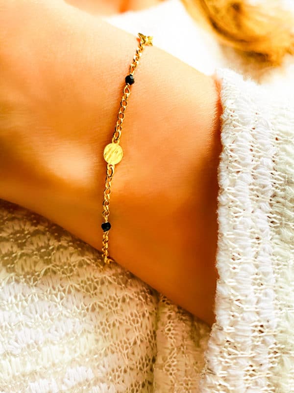 Gros plan poignet de femme avec le bracelet Luna Doré avec une chaîne en plaqué or avec des plaques rondes martelées et des pierres noires