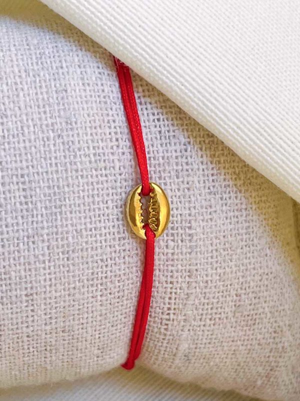 Gros plan sur un tissu blanc un bracelet cordon rouge avec un coquillage plaqué or