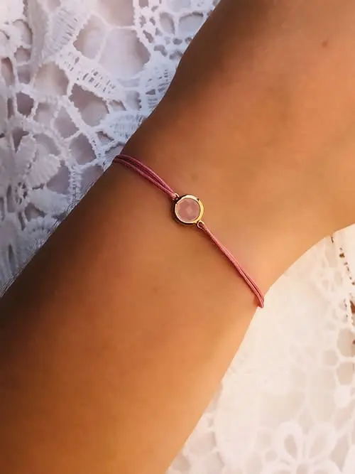 Gros plan poignet de femme avec un bracelet cordon avec une pierre semi précieuse de quartz rose cerclée de plaqué or. Bijoux à personnaliser et fabriqués à la main