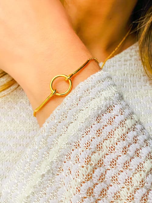 Gros plan poignet de femme avec le bracelet Théa avec une chaîne en plaqué or, un cercle ajouré tenu par deux barres courbées