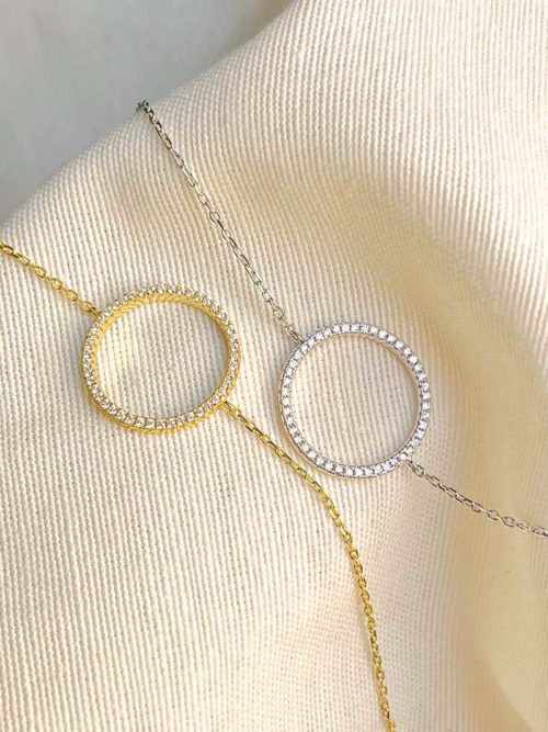 Gros plan posés sur un tissu blanc, deux bracelet chaînes avec un cercle recouvert de zircons l'un en argent l'autres en en plaqué or. Bracelet Soline