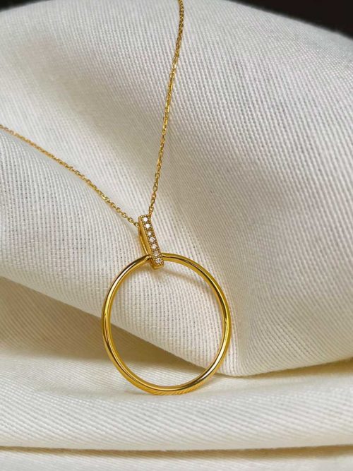 Gros plan collier posé sur un tissu blanc, le collier Lise Doré en plaqué or avec un pendentif en forme de cercle tenu par une baguette de zircon
