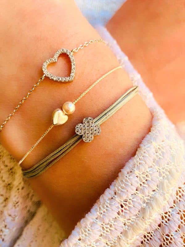 Gros plan poignet penché avec une association de bracelet en argent avec perle et zircons. Bracelet Clara, bracelet Eliya, bracelet cordon Fleur Blanche