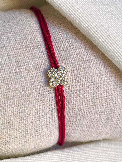 Gros plan sur un tissu blanc un bracelet cordon avec une fleur en plaqué or recouverte de zircons