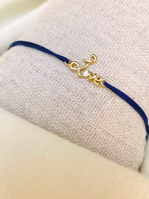 Gros plan sur un tissu blanc un bracelet cordon bleu marine avec un love manuscrit en plaqué or avec un zircon dans le o