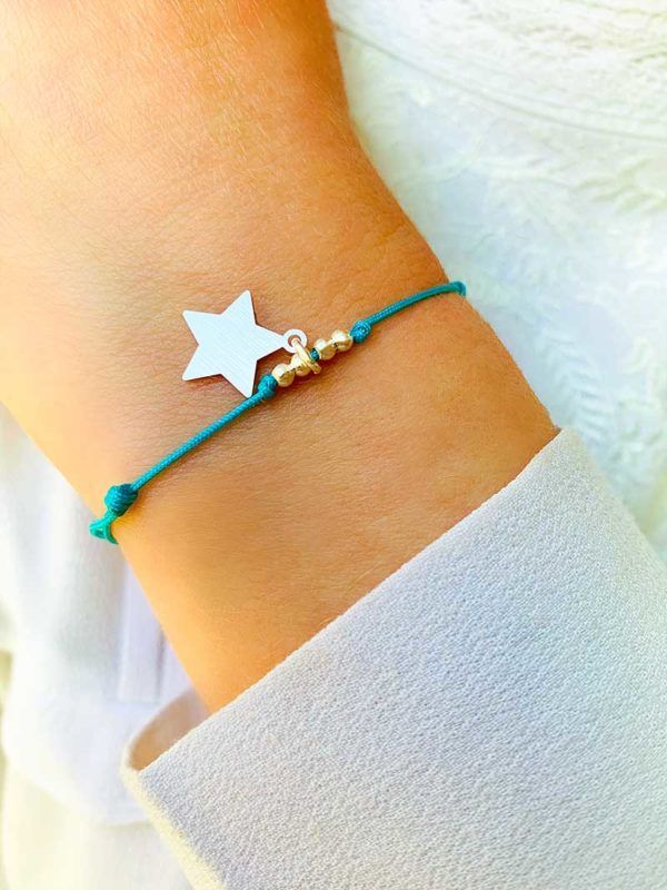 Vue de face gros plan poignet avec bracelet cordon Céline avec un cordon bleu ciel avec un charm en forme d'étoile en argent mat et 4 petites perles en argent