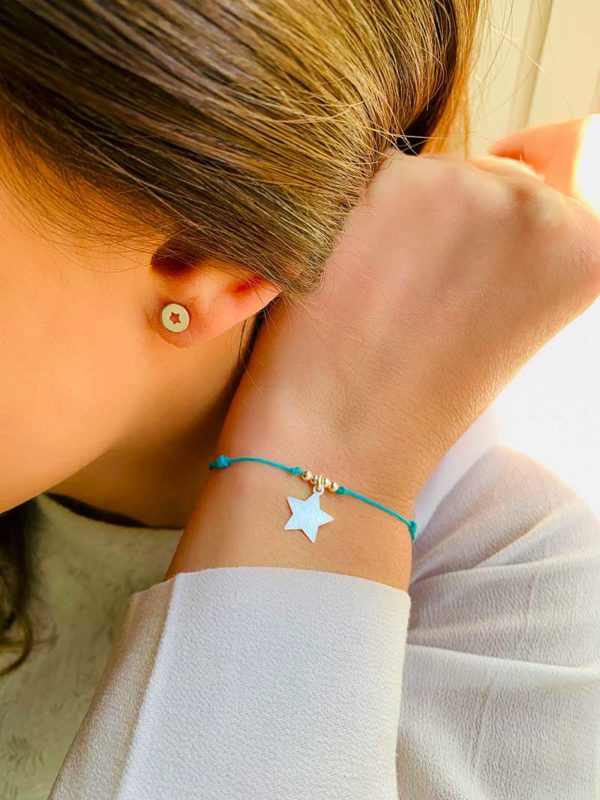 Gros plan de profil oreille avec boucles d'oreilles Lucie en argent avec une étoile ajourée et bracelet cordon Céline avec un charm en étoile et 4 petites perles en argent