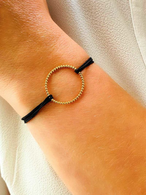 Vue de face gros plan poignet avec le bracelet cordon Emma Doré avec un cercle en forme de petites boules en plaqué or, et un cordon noir. Bracelet réglable et choix de couleur de cordon