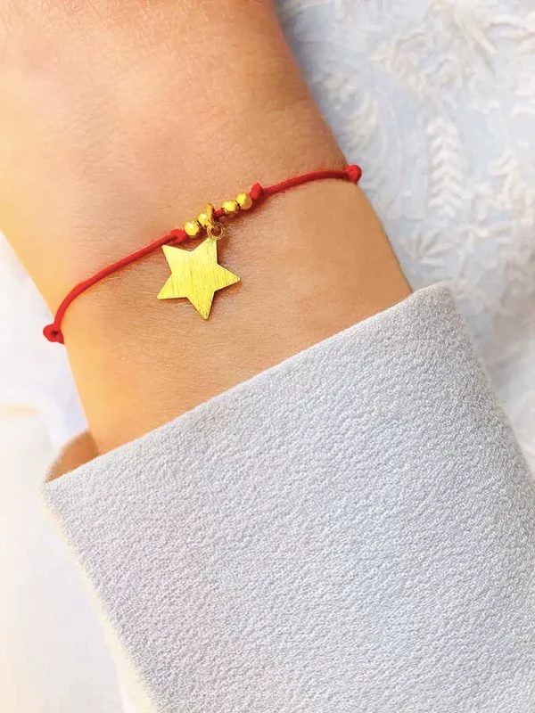 Vue de face gros plan poignet avec bracelet cordon bleu ciel avec un charm en forme d'étoile en argent mat et 4 petites perles en plaqué or