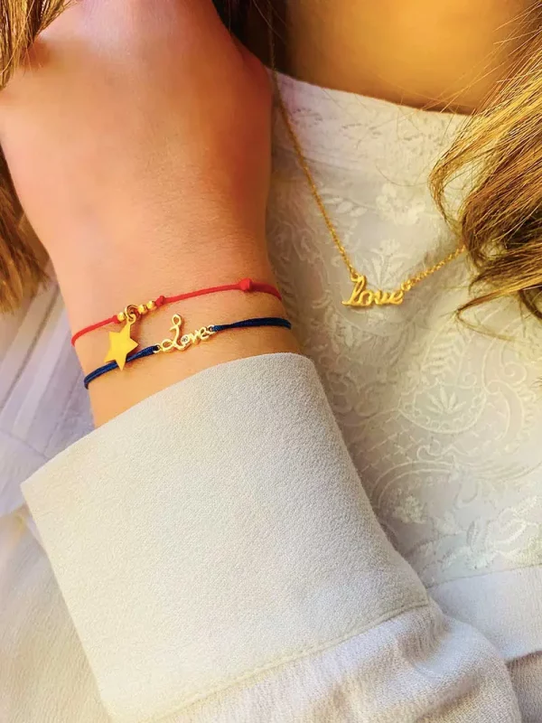 Vue de face buste avec le collier Love en plaqué or avec un love manuscrit, et un poignet penché avec deux bracelets. Le bracelet cordonLove Doré avec un love manuscrit avec zircon et le bracelet cordon Céline Doré une étoile pendante entourée de petites perles tout en plaqué or
