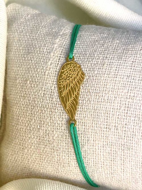 Gros plan sur un tissu blanc un bracelet cordon vert avec une aile d'ange gravée en plaqué or