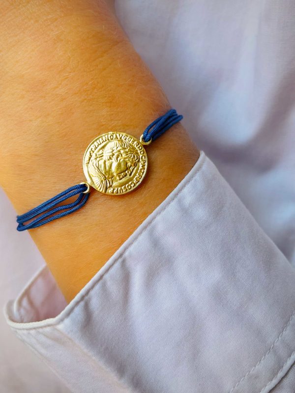 Gros plan poignet avec le bracelet cordon Romane avec une pièce romaine gravée en plaqué or. Bijoux personnalisables