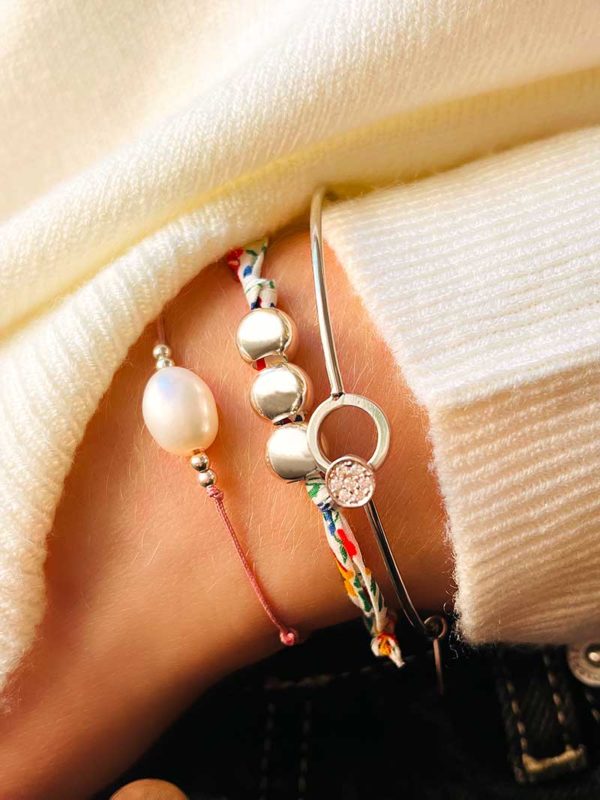 Gros plan d'une main dans un jean avec 3 bracelets au poignet. Le bracelet cordon Oriane avec une perle baroque, le bracelet cordon Charlotte avec 3 grosses perles en argent. Et le bracelet Laura, un jonc en argent avec une plaque ronde recouverte de zircons