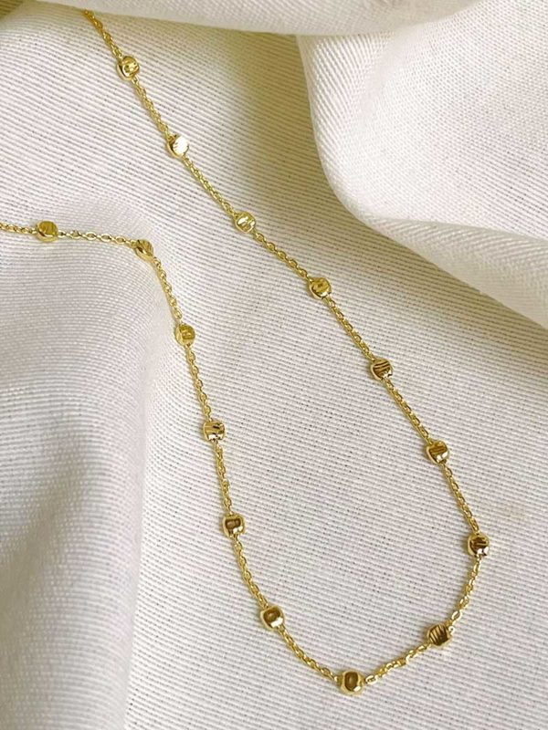 Gros plan sur un tissu blanc le collier Emilie Doré en plaqué or sur une fine chaîne des petites plaques rondes martelées