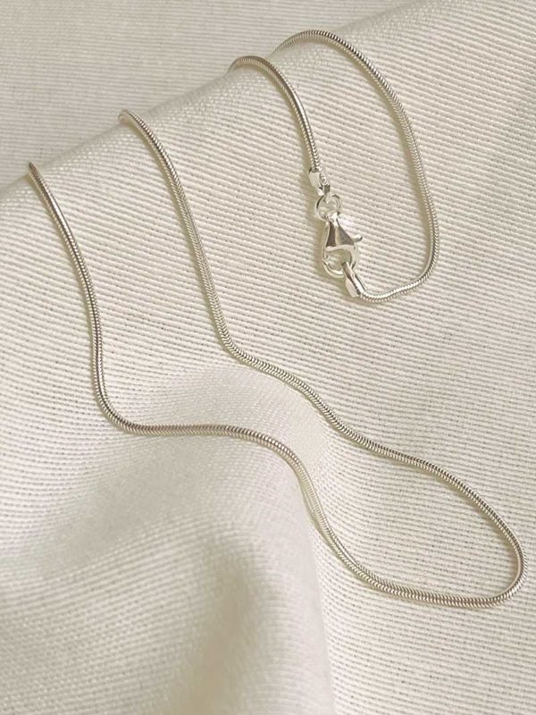 Gros plan sur un tissu blanc un collier en argent avec une maille serpent