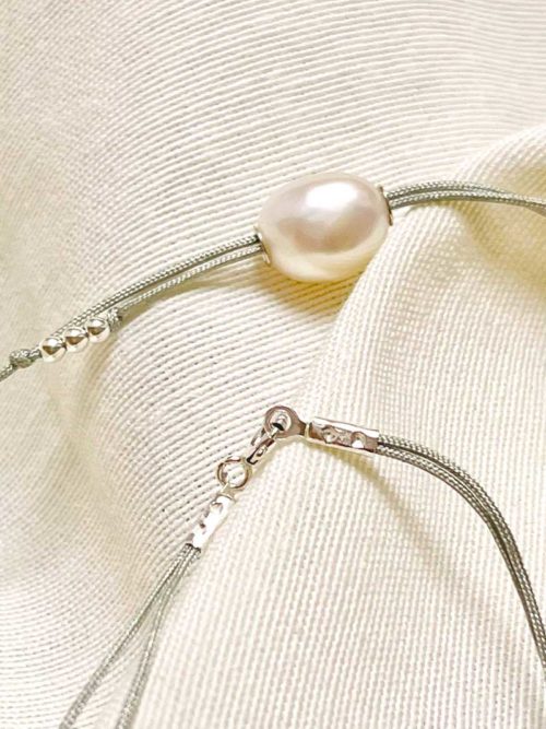 Gros plan sur un tissu blanc un collier avec une perle baroque et un double cordon de couleur en coton. Bijoux en argent