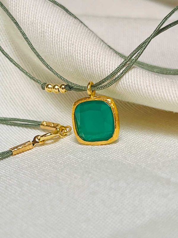 Gros plan posé sur un tissu blanc le collier cordon Chloé avec un pendentif de forme carré avec une pierre semi précieuse en onyx vert