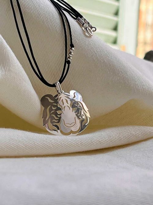 Gros plan sur un tissu blanc du collier cordon Inaya avec un pendentif en forme de tête de tigre en argent