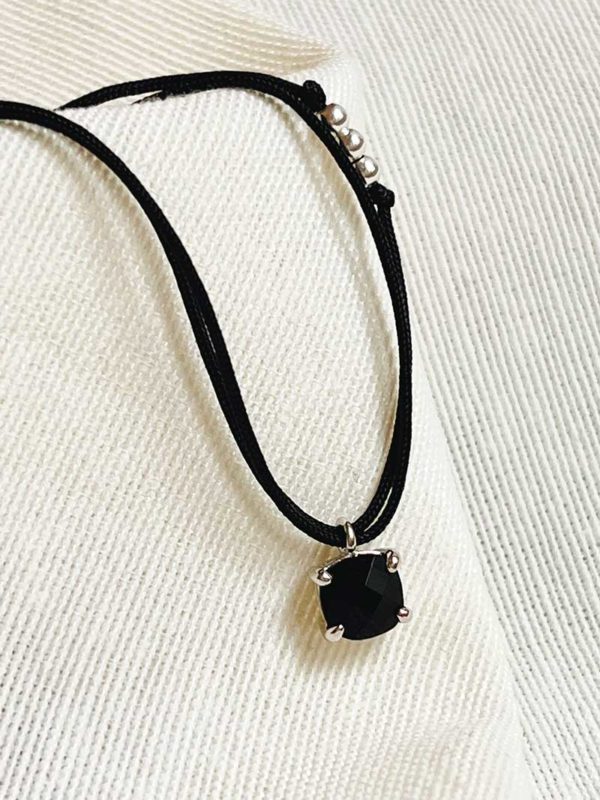 Gros plan sur un tissu blanc le collier cordon Léa avec une pierre semi précieuse d'agate noir et un double cordon de couleur en coton. Bijoux en argent