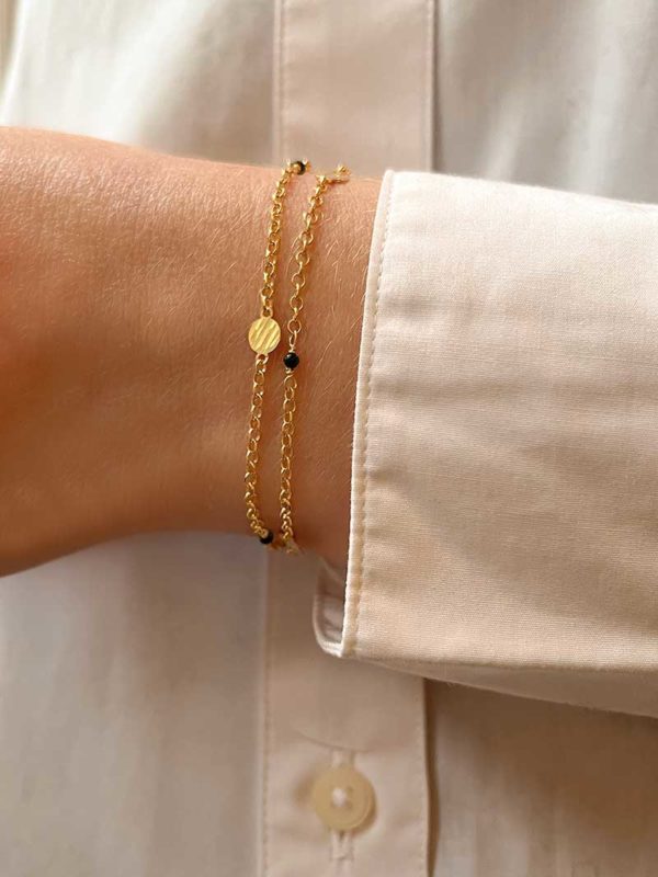 Gros plan poignet de femme avec un double bracelet en plaqué or avec des plaques martelées et des pierres noires