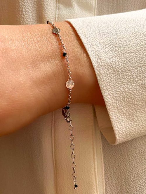 Gros plan poignet de femme avec le bracelet Luna avec une chaîne en argent avec des plaques rondes martelées et des pierres noires