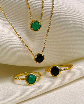 sur un tissu blanc le collier Jeanne en plaqué or avec une pierre ronde d'onyx noir ou vert
