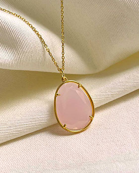 Gros plan collier posé sur un tissu blanc, le collier Maelys est en plaqué or avec une pierre ovale en quartz rose