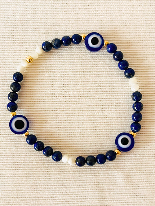 Gros plan bracelet élastique pierre naturelle lapis-lazuli nacre perles dorées oeil bleu porte-bonheur