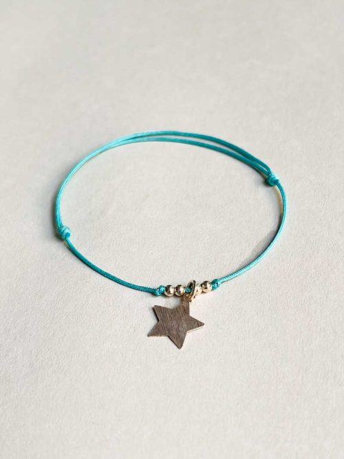 Gros plan posé devant un fond blanc le bracelet cordon Céline avec une étoile en argent mat et un cordon bleu ciel