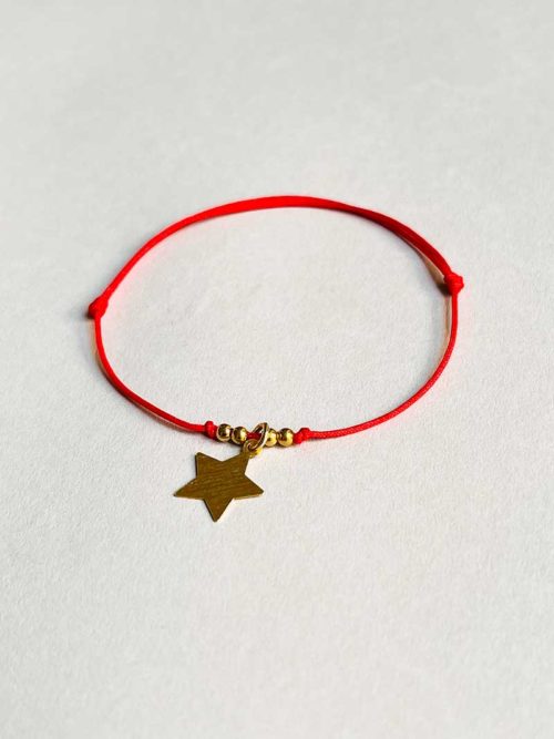 Gros plan posé devant un fond blanc le bracelet cordon Céline Doré avec une étoile en plaqué or mat et un cordon rouge