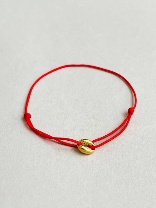 Gros plan posé devant un fond blanc le bracelet cordon Coquillage Doré avec un coquillage en plaqué or et un cordon rouge