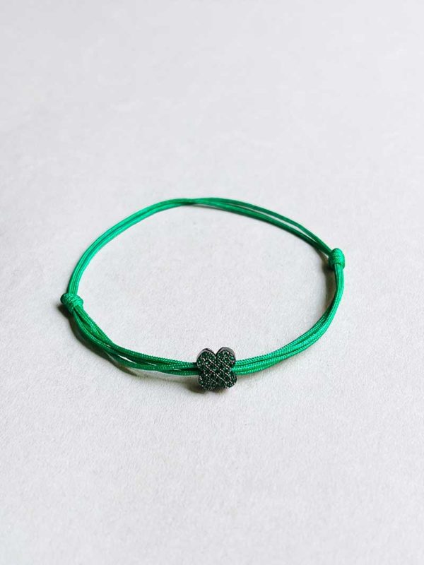 Gros plan posé devant un fond blanc le bracelet cordon Fleur Verte avec une fleur en argent noir recouverte de zircons verts et un double cordon vert
