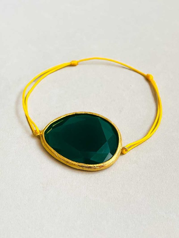 Gros plan posé devant un fond blanc le bracelet cordon Grand Delta Vert avec une pierre semi précieuse d'onyx vert cerclée de plaqué or et un cordon jaune