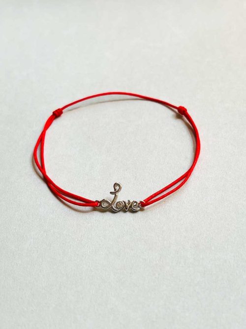 Gros plan posé devant un fond blanc le bracelet cordon Love avec un love manuscrit en argent surmonté d'un zircon et un cordon rouge