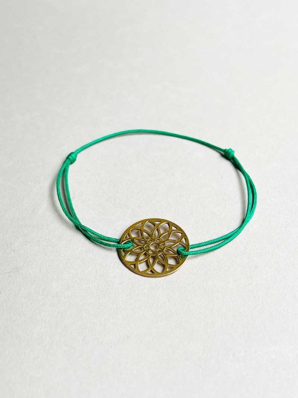 Gros plan posé devant un fond blanc le bracelet cordon Mandala Doré avec un mandala en plaqué or et un cordon vert